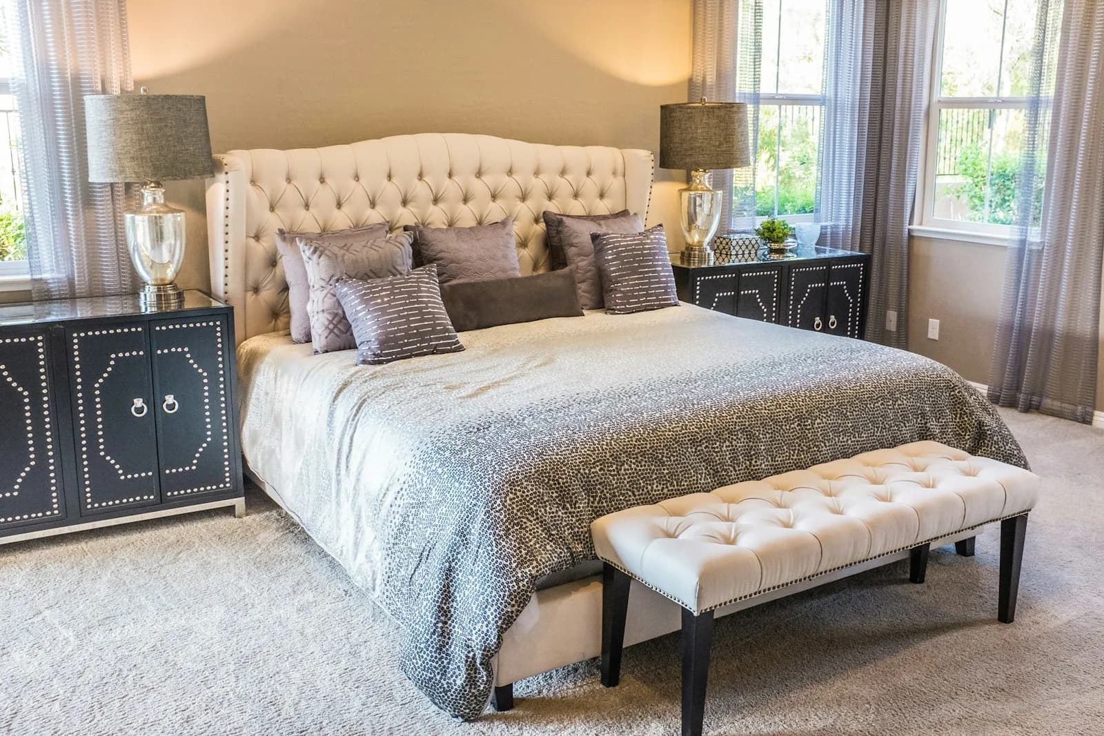 A bright bedroom with white bedding, wood floors, and daylight from tall windows.