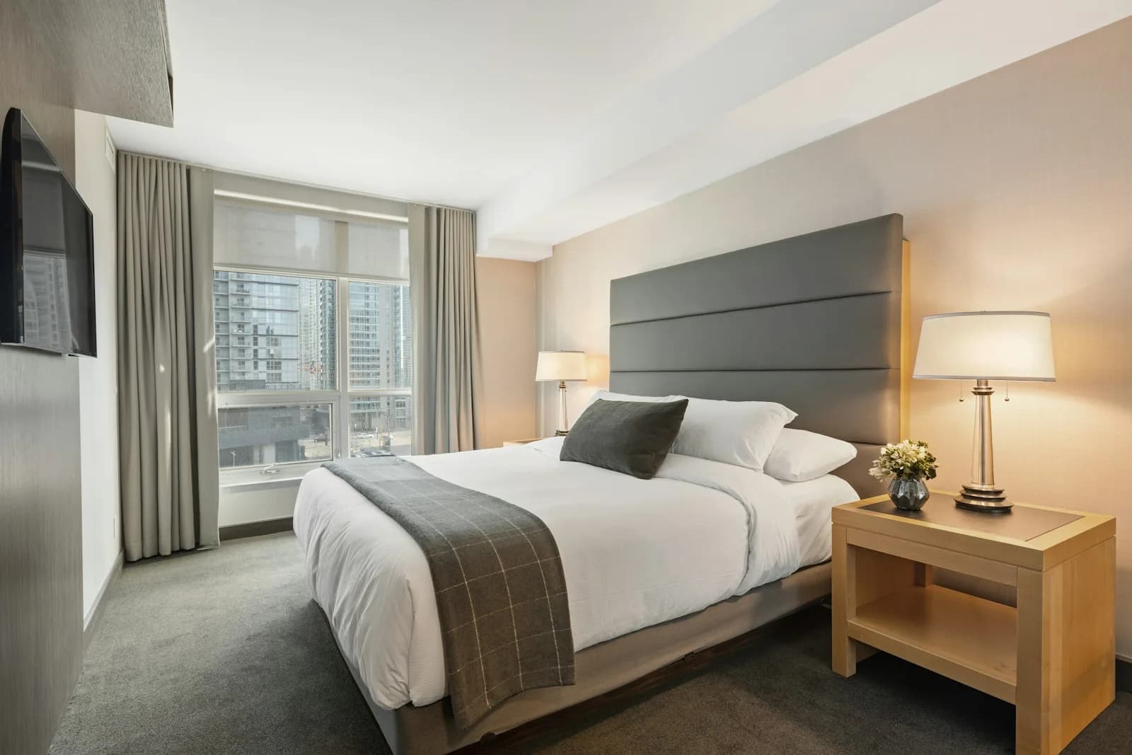 A bright bedroom with white linens, a wood headboard, and morning light.