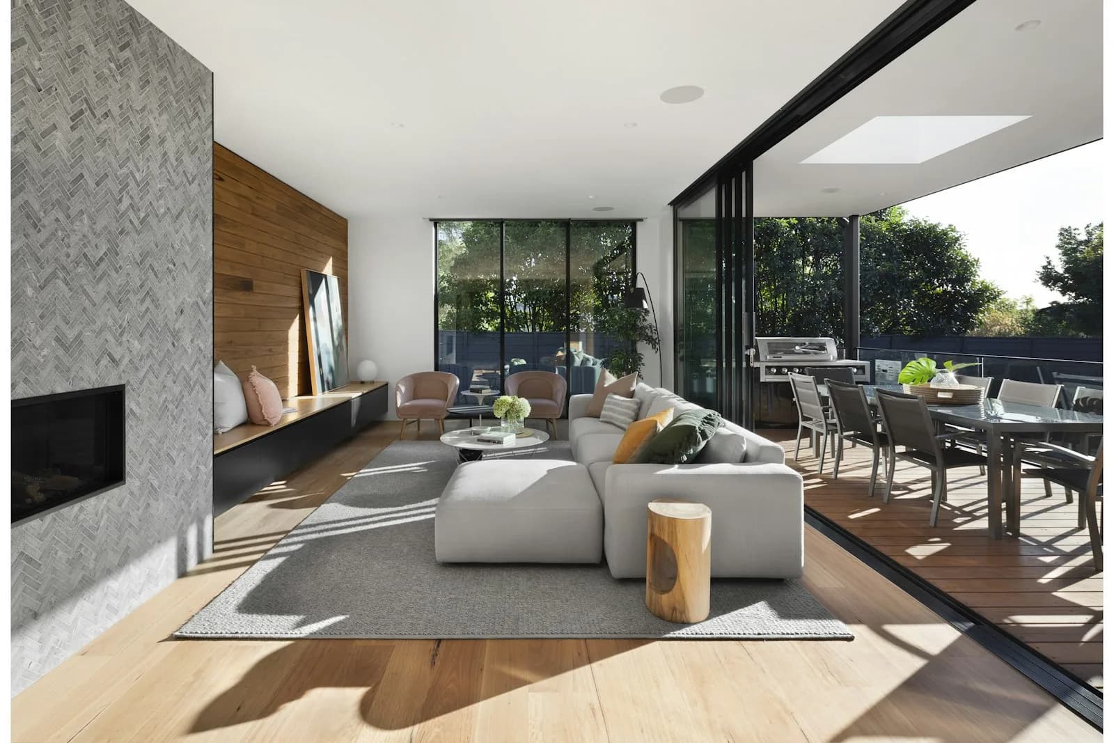 A bright living room with a gray sectional, wood floors, and doors open to a deck.