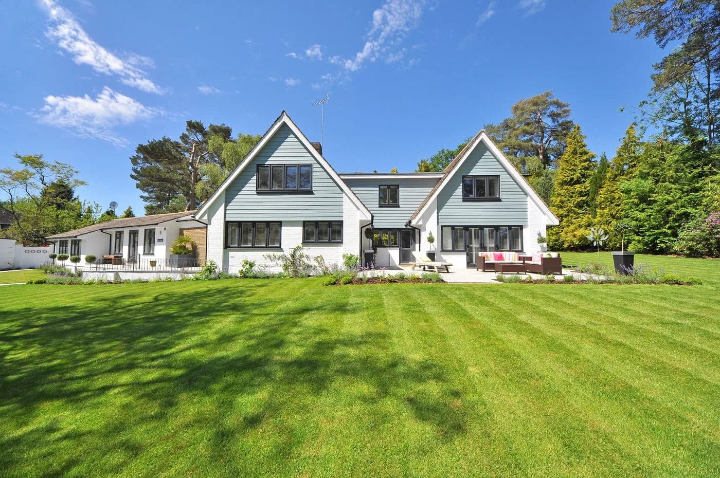 A two-story house with a green lawn, dark windows, and a clear blue sky.