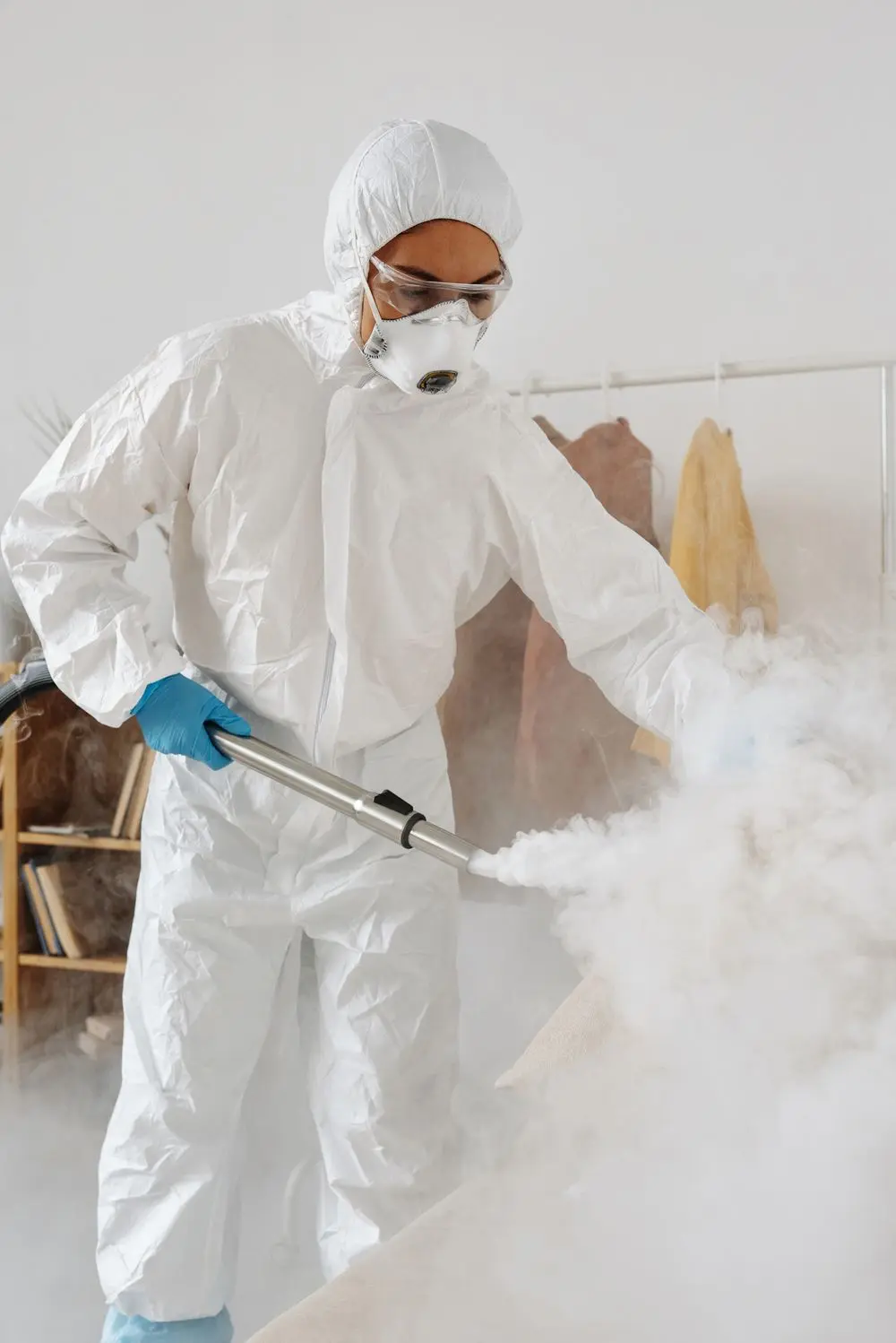 A technician in a white suit spraying across a bright room.